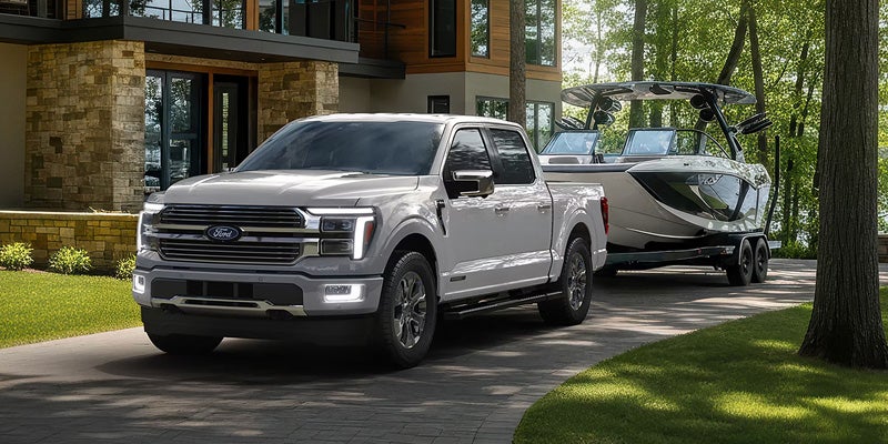 Silver Ford F-150 towing a boat along a wooded driveway.
